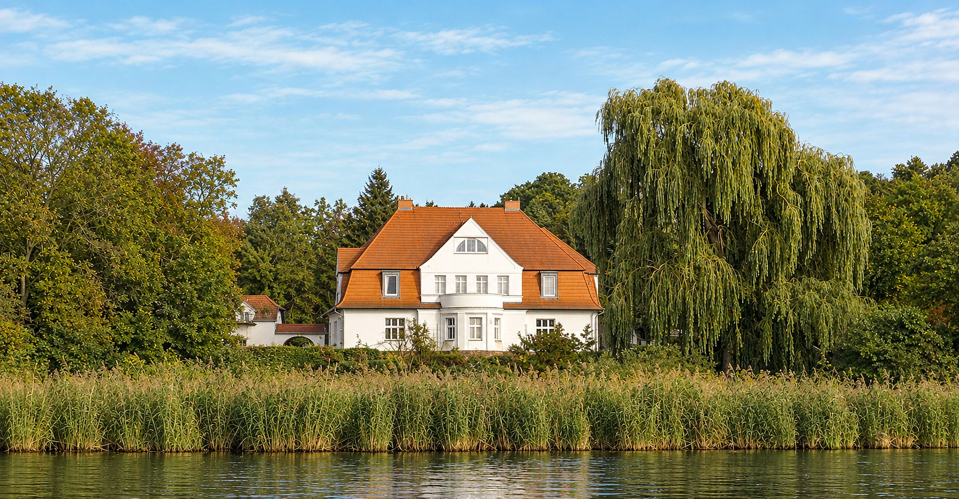 Der Gutshof Schwielowsee vom Wasser aus gesehen, mit Schilfgürtel im Vordergrund