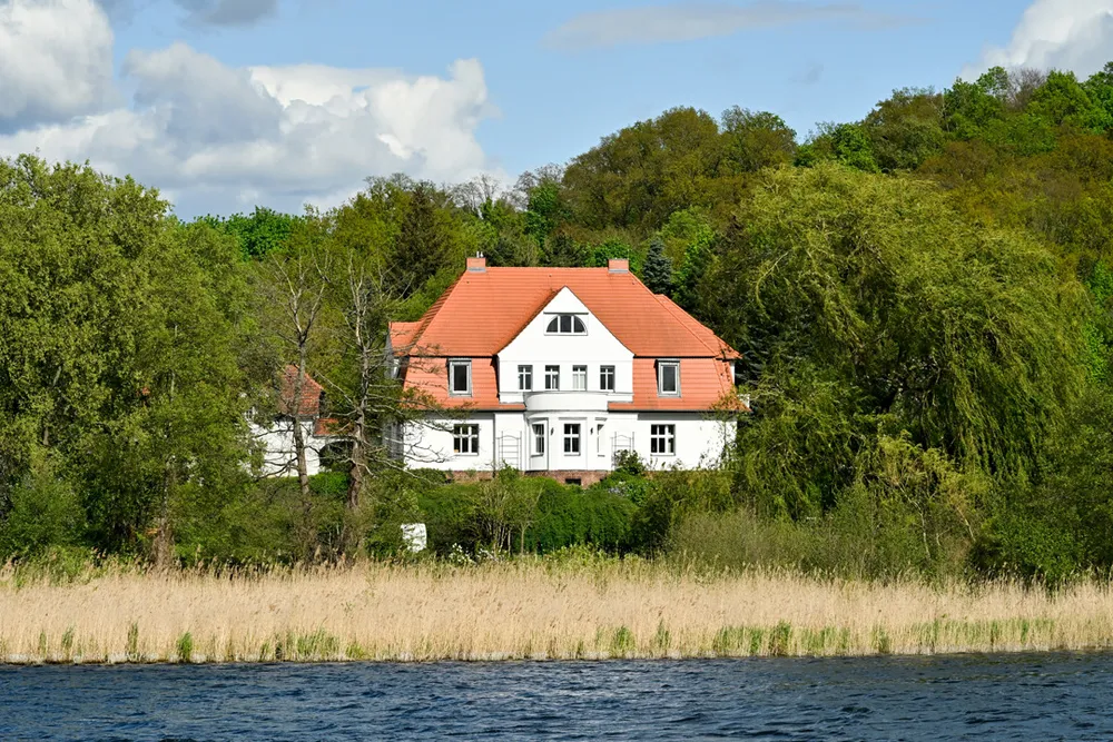 Der Gutshof vom Wasser aus gesehen, mit Schilfgürtel im Vordergrund